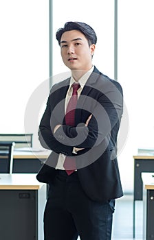 Millennial Asian young professional successful male businessman manager in formal suit standing smiling crossed arms thinking in