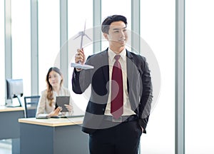 Millennial Asian young professional successful male businessman manager in formal suit standing smiling holding windmill model