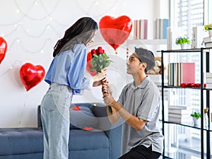 Millennial Asian young romantic lover couple male boyfriend kneel down giving red roses bouquet surprising female girlfriend