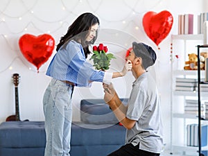 Millennial Asian young romantic lover couple male boyfriend kneel down giving red roses bouquet surprising female girlfriend