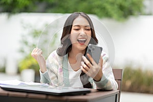 Millennial asian young woman looking mobile phone laughing with good news or discount voucher for shopping online at home.Happy