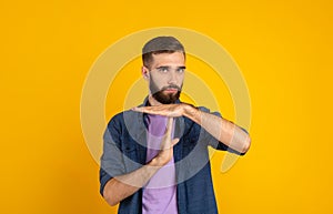 Millennial bearded guy showing TIME OUT or STOP gesture over orange studio background