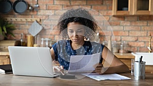 Millennial biracial woman manage household finances in kitchen