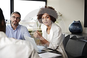 Millennial black businesswoman listening to colleagues at a corporate business meeting, close up