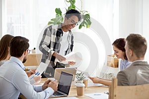 Millennial black female share paperwork handouts at office meeti