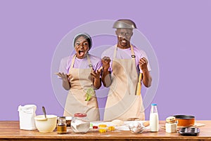 Millennial black girl and her boyfriend shouting from anger while attempting to bake on lilac background