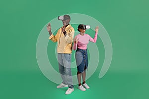 Millennial black guy and woman using VR glasses, green background