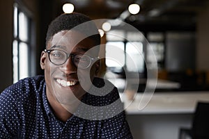 Millennial black male creative sitting at a desk in an office smiling to camera, close up photo