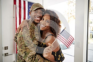 Millennial African American  soldier and wife embracing at home and smiling to camera,waving flag, close up