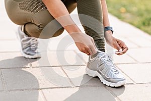 Millennial black sportswoman tying laces of her shoes while jogging at park, close up of legs