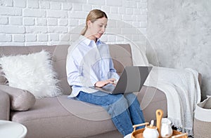 Millennial business woman using laptop sitting on couch in living room