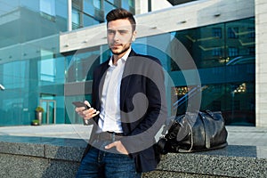 Millennial businessman with a mobile phone in his hands. Young successful business stylish man with a black leather bag