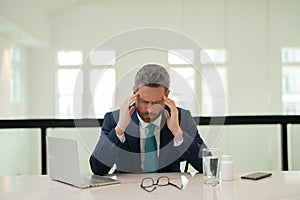 Millennial Businessman in office having headache. Business man in suit work on laptop at home office take off glasses