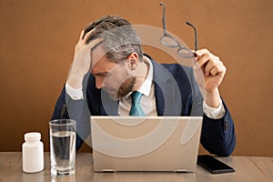 Millennial Businessman in office having headache. Business man in suit work on laptop at home office take off glasses