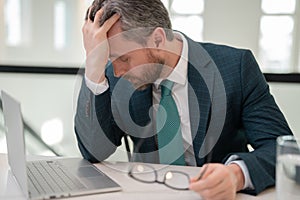 Millennial Businessman in office having headache. Business man in suit work on laptop at home office take off glasses