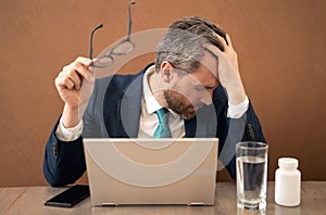 Millennial Businessman in office having headache. Business man in suit work on laptop at home office take off glasses