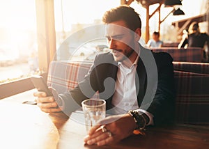 Millennial businessman sitting in a cafe at a table and looking at the screen of his mobile phone.