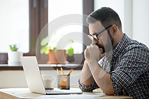 Millennial casual businessman thinking and looking at laptop in