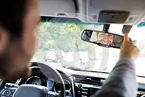 Millennial caucasian guy in suit with hands on steering wheel, configures mirror