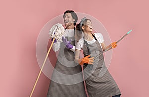 Millennial couple having fun during spring cleaning, using broom like air guitar and singing into mop