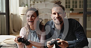 Millennial couple holding controllers playing video games seated on couch