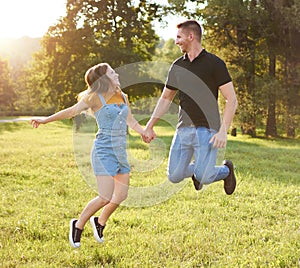 Millennial couple holding each other`s hand and jumping together outdoors in a park - Happy people lifestyle concept