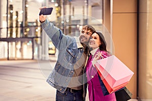 Millennial couple joyfully taking a selfie on smartphone outside mall