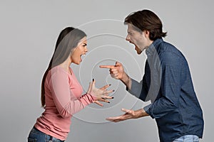 Millennial couple quarreling, shouting and blaming each other over light background