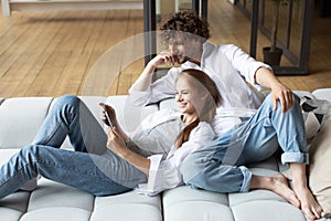 Millennial couple relax on couch using digital tablet together at home sitting on sofa