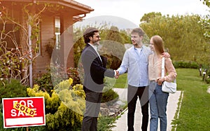 Millennial couple shaking hands with real estate agent near their new house outdoors, copy space