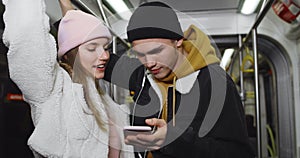 Millennial couple talking and looking at mobilephone screen. Pretty girl and her boyfriend sharing headphones and