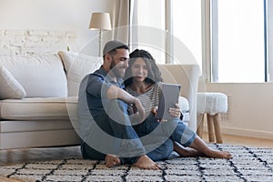 Millennial couple using digital tablet seated on floor at home