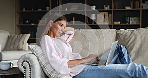 Millennial female writer recline on couch type text on laptop