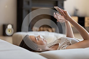 Millennial girl resting on sofa using smartphone gadget