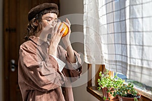 Millennial girl smelling orange with closed eyes while standing by window at home