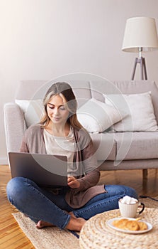 Millennial girl typing on laptop, studying on floor at home