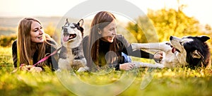 Millennial girls playing with their siberian husky dogs outdoors in the grass - Owners and their pets having fun together - Dog