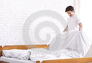 Millennial guy making bed in morning, domestic chores concept