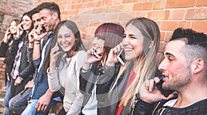 Millennial guys and girls using mobile smart phone and having fun at brick stone wall in the city - Urban youth and technology