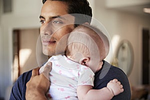 Millennial Hispanic father holding his newborn son close to his chest, head and shoulders, close up