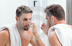 Millennial hispanic man looking in mirror, facial skin and stubble. Male beauty care product. Skincare, home spa. Beauty