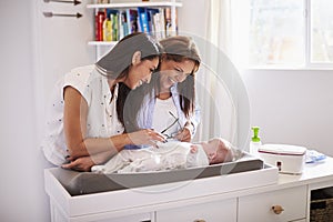 Millennial Hispanic mother and grandmother playing with baby son on changing table, selective focus
