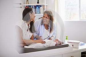 Millennial Hispanic mother and grandmother playing with baby son on changing table, selective focus