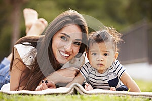 Millennial Hispanic mother lying on a blanket in the park with her baby, smiling to camera, close up