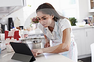 Millennial Hispanic woman preparing cake mixture checking the recipe on her tablet computer