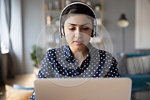 Millennial Indian girl in headphones study on laptop