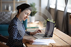 Millennial Indian girl study at laptop making notes