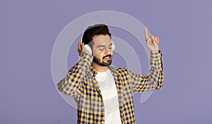 Millennial Indian music lover enjoying his favorite songs in headphones on violet background