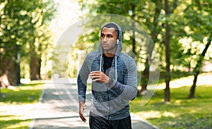 Millennial jogger with earphones enjoying his morning run at summer park, empty space