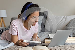 Millennial lady lie by laptop in headset listen to teacher